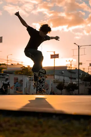 Young skateboarder performs a trick against a vibrant sunset backdrop.