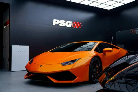 Orange Lamborghini Huracan parked indoors with PSG logo overhead, showcasing luxury and power.