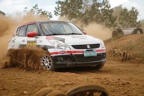 High-speed rally car kicking up dust on a dirt track during a race event.