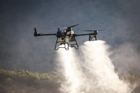 A drone dispersing spray over a green field, showcasing modern agricultural technology and crop management.
