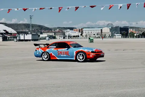 A stylish drifting car on an open asphalt track in Turkey with clear skies and flag decorations.