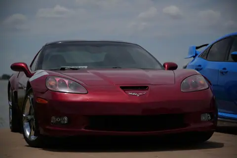 Front view of a red sports car with a blue car parked beside it, outdoors under clear skies.