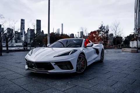 A stylish white sports car parked in a city backdrop during fall.