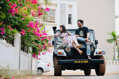 A joyful couple sitting on a black jeep surrounded by vibrant flowers, capturing a moment of happiness.