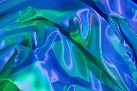 A vivid and colorful satin fabric with ripples and folds in blue and green hues.