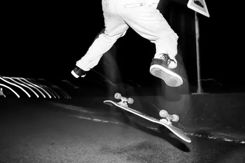 Black and white action shot of a skateboarder performing a trick at night, highlighting motion and energy.