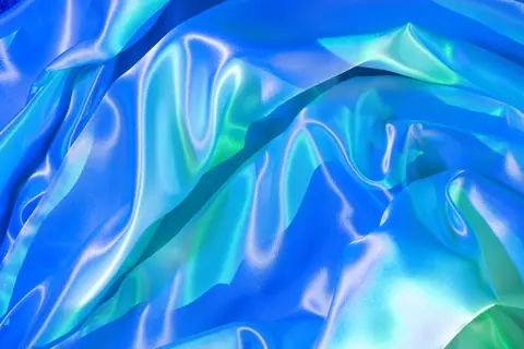 A close-up view of vibrant satin silk fabric with elegant blue and green reflections, creating a luxurious abstract texture.