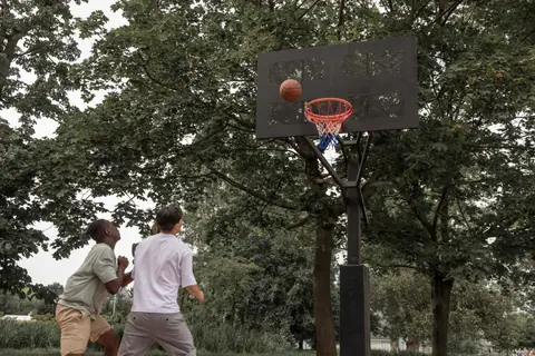 Unrecognizable diverse sportsmen in activewear throwing ball in hoop while playing basketball on sports ground in summer park