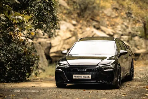Sleek black luxury car against a natural autumn backdrop, showcasing elegance and design.