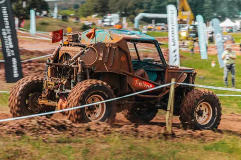 Intense offroad racing scene with a rugged buggy maneuvering through muddy terrain on a track.