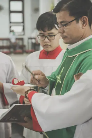 Priest performing a holy ceremony with altar servers holding a book inside a church.
