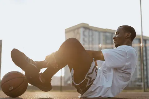 A young basketball player relaxing on an outdoor court during sunset.