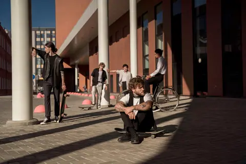 Group of young adults with skateboards and bike in a cityscape with modern architecture.