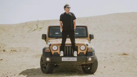 Confident man in sunglasses standing on a rugged SUV in a vast desert setting.