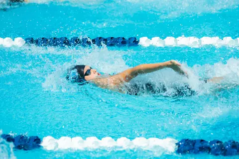 A professional swimmer performs the backstroke during a competitive race in an outdoor pool.