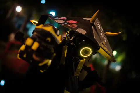 A person in neon cyberpunk costume poses dramatically at night.