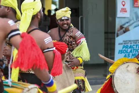 Colorful drummers perform at a lively outdoor festival, showcasing traditional costumes and vibrant music.