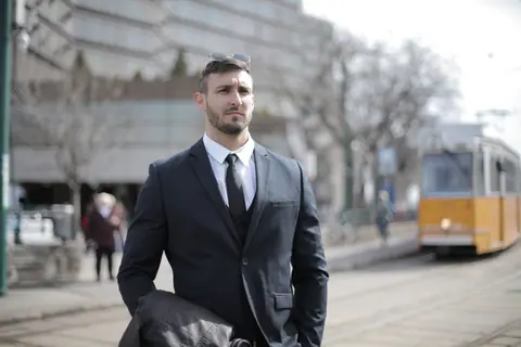 A serious businessman in a suit stands outdoors near a tram track.