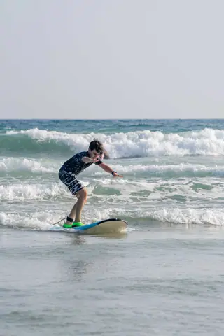 A young boy surfing on waves during a sunny summer day at the beach.