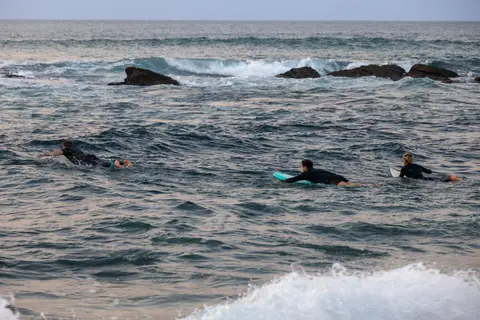 Three surfers paddle out into ocean waves, ready to catch some surf on a calm day.