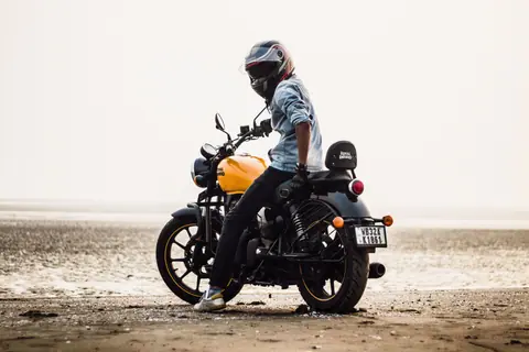 Man wearing helmet on Royal Enfield bike at the beach, exuding freedom and adventure.