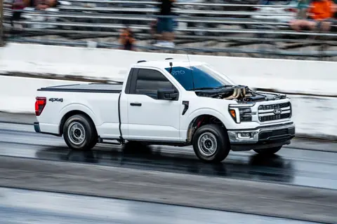 White pickup truck racing on track, showcasing speed and power at drag race event.