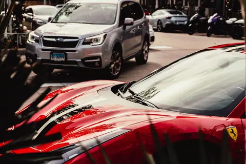 A striking red luxury sports car parked on a city street alongside other vehicles.