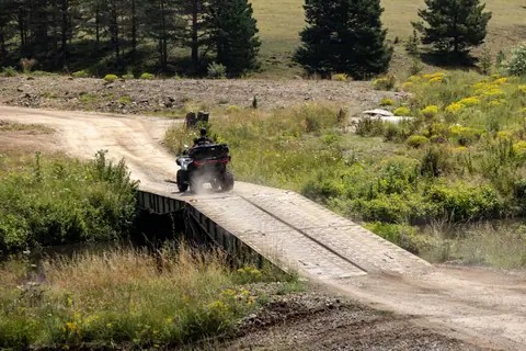 An ATV crosses a rustic bridge surrounded by lush greenery in the sunny Zlatibor region of Serbia.