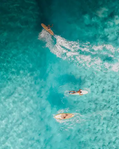 Captivating aerial shot of surfers riding turquoise waves in the ocean, ideal for summer vacation themes.
