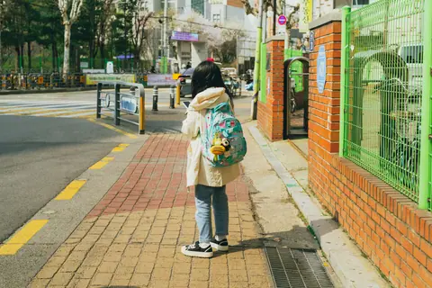 A child wearing a backpack stands on a colorful pavement in Seoul, capturing a peaceful spring day in the city.