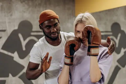 Boxing coach instructing a focused female trainee in a gym setting. Intense training moment captured.