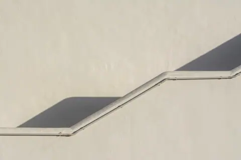 Elegant minimalist stucco wall with stairs casting geometric shadows, emphasizing simplicity.
