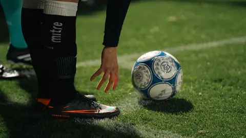 A soccer player in athletic gear prepares for a throw-in during a nighttime match on a grassy field.