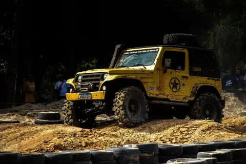 Yellow off-road vehicle navigating through a rugged, muddy terrain during an outdoor challenge event.