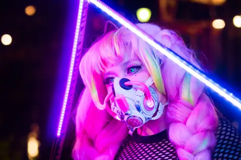 Cosplayer in neon lighting with cyberpunk mask at night, capturing a futuristic aesthetic.