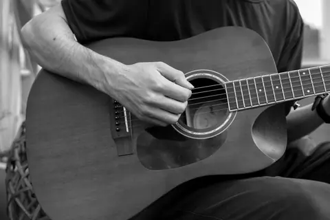 Black and white image of a musician strumming an acoustic guitar, focusing on hands and strings.