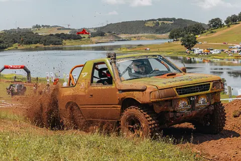 A rugged off-road truck kicks up mud during a thrilling race near a picturesque lake.