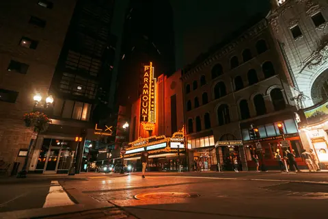 A nighttime street scene featuring the iconic Paramount Theater in Boston, illuminated by bright neon lights.
