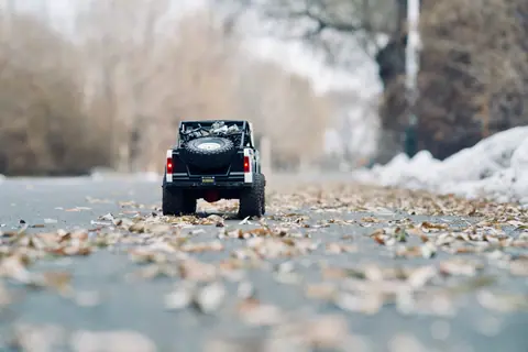 Miniature toy car on an autumn road with scattered leaves, showcasing detail and seasonal charm.