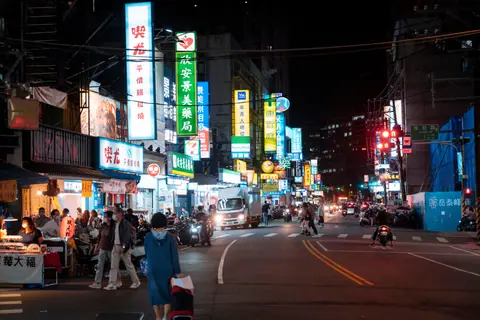 Vibrant night market scene featuring neon signs, people walking, and a lively atmosphere.