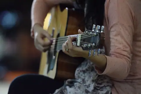 A woman skillfully playing an acoustic guitar, showcasing her musical performance talent.