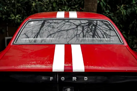 Close-up of a red vintage Ford Mustang featuring white racing stripes and a classic design.