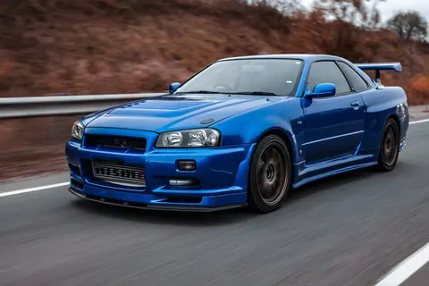 Close-up of a sleek blue Nissan Skyline GT-R driving on a scenic road.