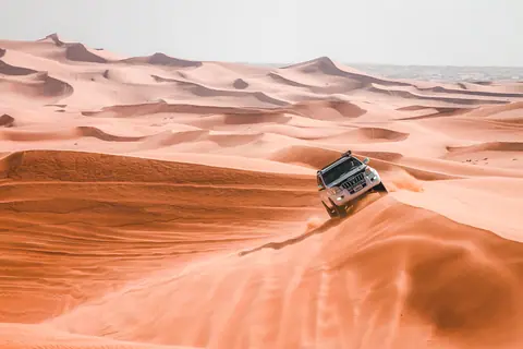 A sports utility vehicle embarks on a thrilling desert safari, navigating vast sand dunes under bright daylight.