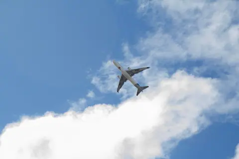 A commercial airplane soars through a bright blue sky filled with fluffy clouds, viewed from below.