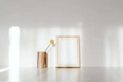 Minimalist photo frame and vase on a white surface with natural shadows.