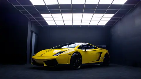 A sleek yellow Lamborghini Gallardo sports car in a minimalist indoor garage setting.