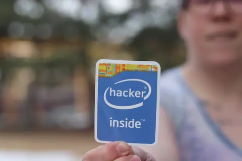 Person holding a 'hacker inside' sticker in an outdoor setting with blurred background.
