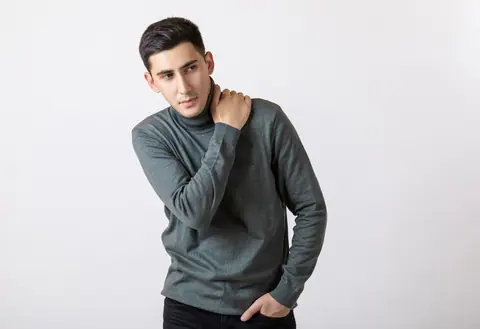 Young man in a gray turtleneck sweater posing in a studio setting.