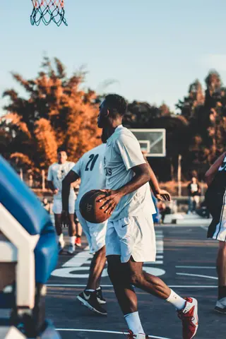 Group of men playing basketball outdoors during sunset, showcasing teamwork and action.